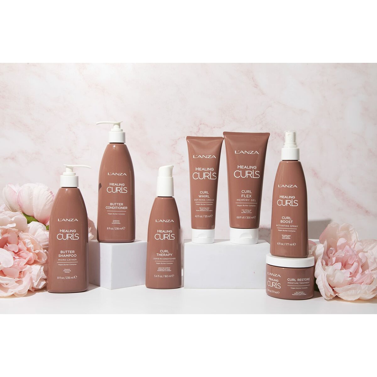 L'ANZA Healing Curls hair care products displayed with pink flowers, featuring butter shampoo, conditioner, and styling cream.