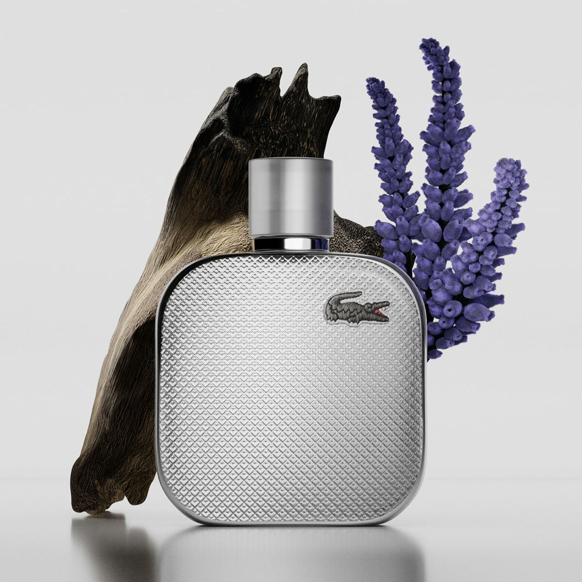Bouteille de parfum homme Lacoste L. 12.12 POUR LUI avec fleurs et bois sur fond neutre.