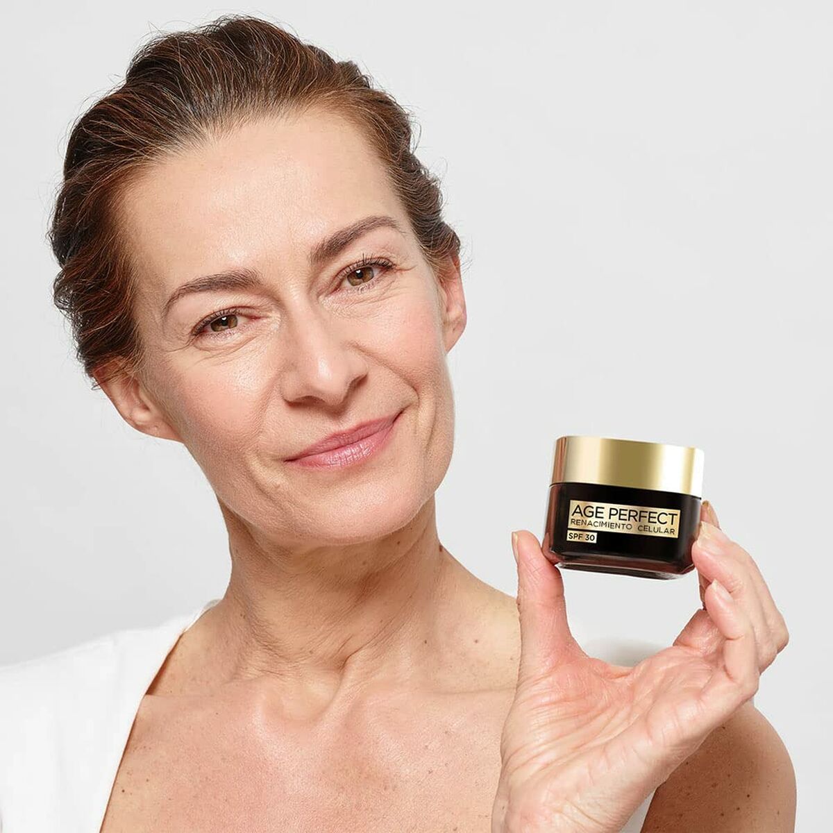 Femme présentant la crème visage L'Oreal Age Perfect Cell Renewal SPF 30, mettant en avant sa texture et son efficacité.