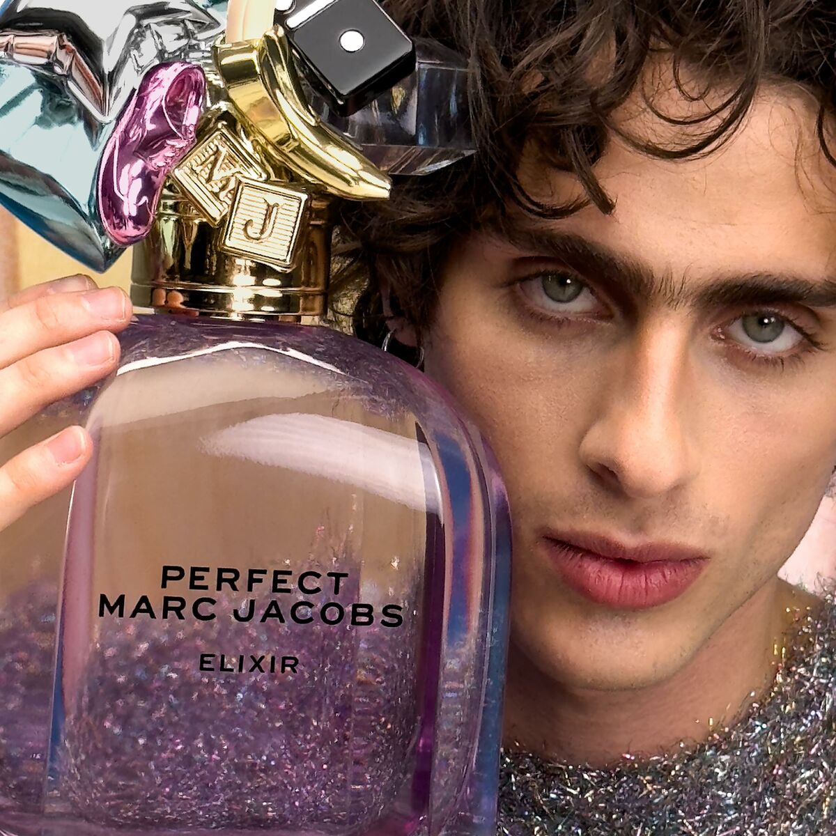 Parfum Unisexe Marc Jacobs PERFECT Elixir 50 ml avec un homme, flacon violet avec paillettes et bouchon doré.