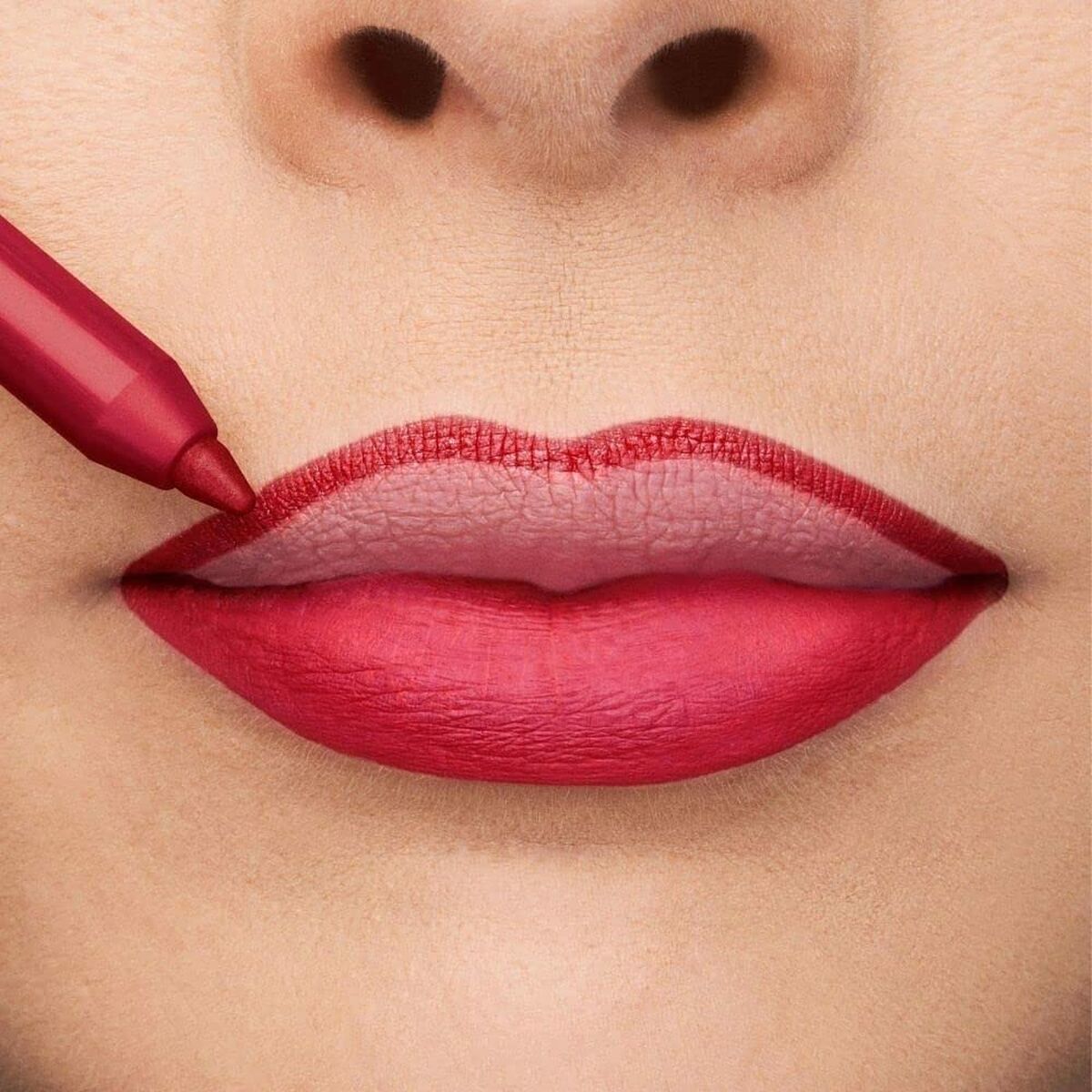 Close-up of lips being lined with a red lip pencil, showcasing a vibrant pink-red lipstick color.