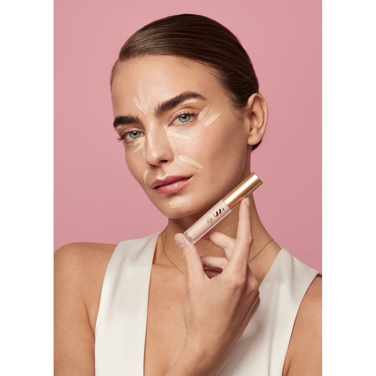 Model applying Éclaircissant Sensilis SKIN GLOW FACIAL with visible facial product and a soft pink background.