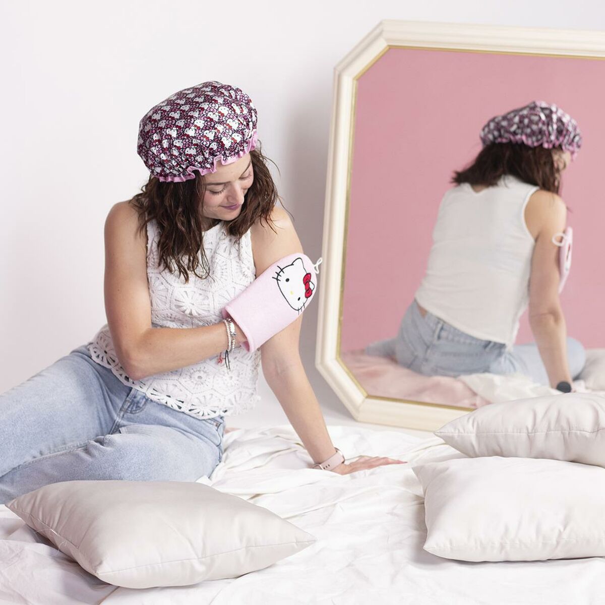 Femme utilisant un gant de toilette Hello Kitty rose, assise sur des coussins avec un miroir en arrière-plan.