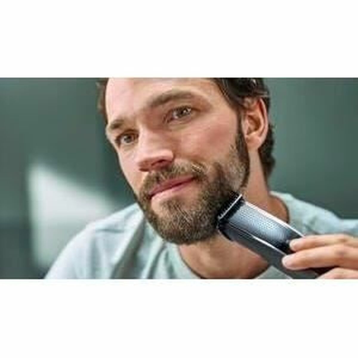 Homme utilisant une tondeuse sur sa barbe, d'apparence soignée, dans un cadre moderne.