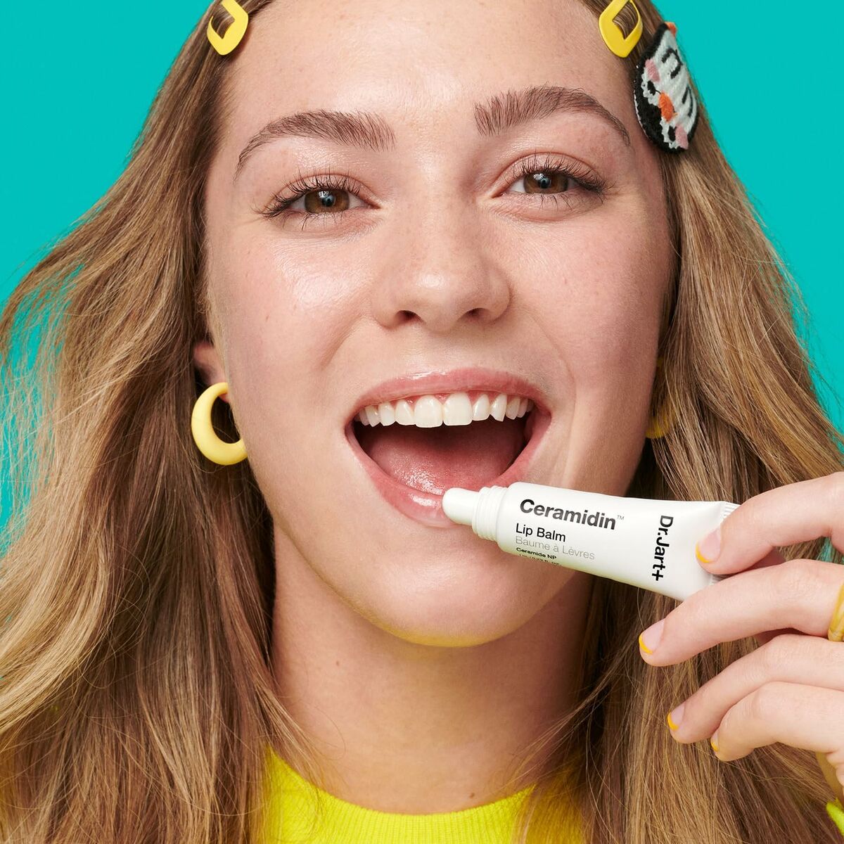 Young woman applying DR.JART+ Ceramidin lip balm, smiling brightly with vibrant background.